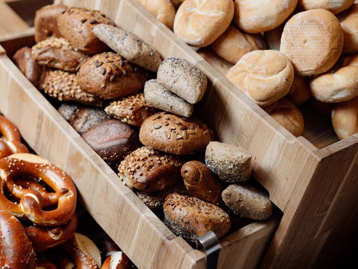 Holzkörbe mit Brezen, hellen Semmeln und Vollkorngebäck mit Sesam, Mohn und Kürbiskernen am Frühstücksbuffet.