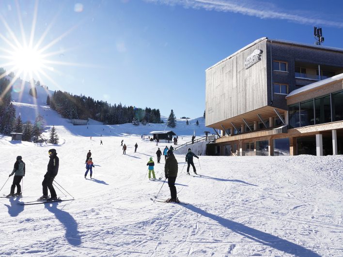 Skifahrer auf der sonnigen Piste der Alpenarena Hochhäderich, die direkt am Almhotel Hochhäderich auf 1.300 Metern im Bregenzerwald vorbeiführt.