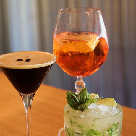 Drei Cocktails an der Wälderbar im Almhotel Hochhäderich, ein Espresso Martini mit Kaffeebohnen, ein Spritz mit Orangenscheibe und ein Mojito mit frischer Minze.