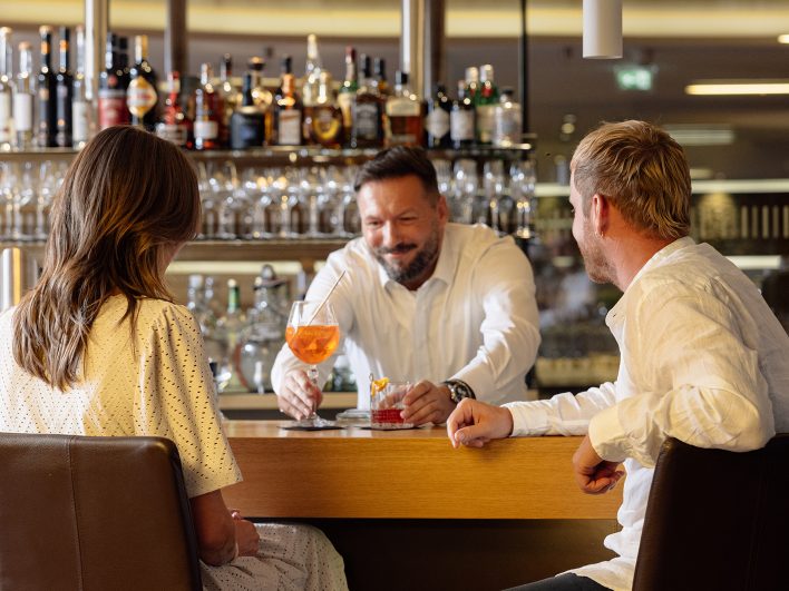 Barkeeper serviert einem Paar an der Theke der Wälderbar zwei Drinks und unterhält sich dabei mit den Gästen.