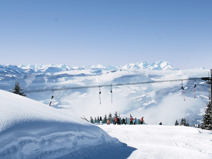 Schlepplift an der Bergstation im Skigebiet am Hochhäderich, Skifahrer genießen die Aussicht über ein Nebelmeer bis zu den verschneiten Alpengipfeln.