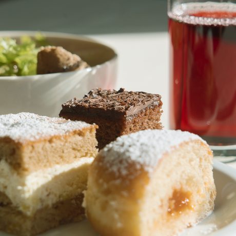 Süße Leckereien der Almjause im Almhotel Hochhäderich mit Schokoladenschnitte, Cremeschnitte und gefülltem Hefegebäck, dahinter eine Schale mit Salat und ein Glas roter Saft.