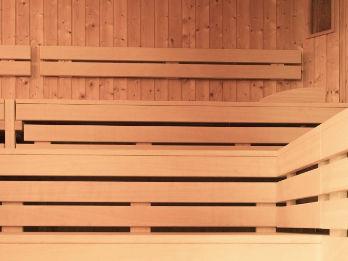 Nahaufnahme der hellen, mehrstufigen Holzbänke in der Sauna des FamSpa, dahinter eine Wand aus warm getöntem Fichtenholz.