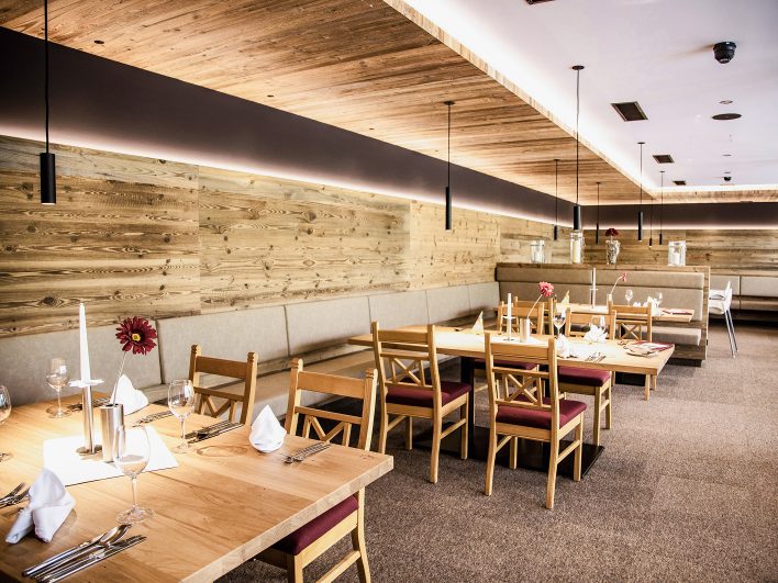 Restaurant Johann & Frieda mit Altholzwand, warmem Licht, Holztischen und Stühlen mit roten Sitzpolstern.