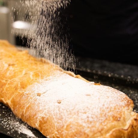 Hausgemachter Apfelstrudel wird frisch aus dem Ofen mit Puderzucker bestäubt, im Tagesrestaurant Johann & Frieda im Almhotel Hochhäderich.