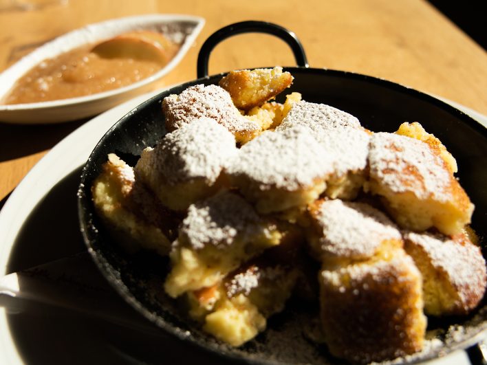Kaiserschmarren mit Puderzucker in der kleinen Pfanne, dazu Apfelmus, auf einem Holztisch in der Sonne