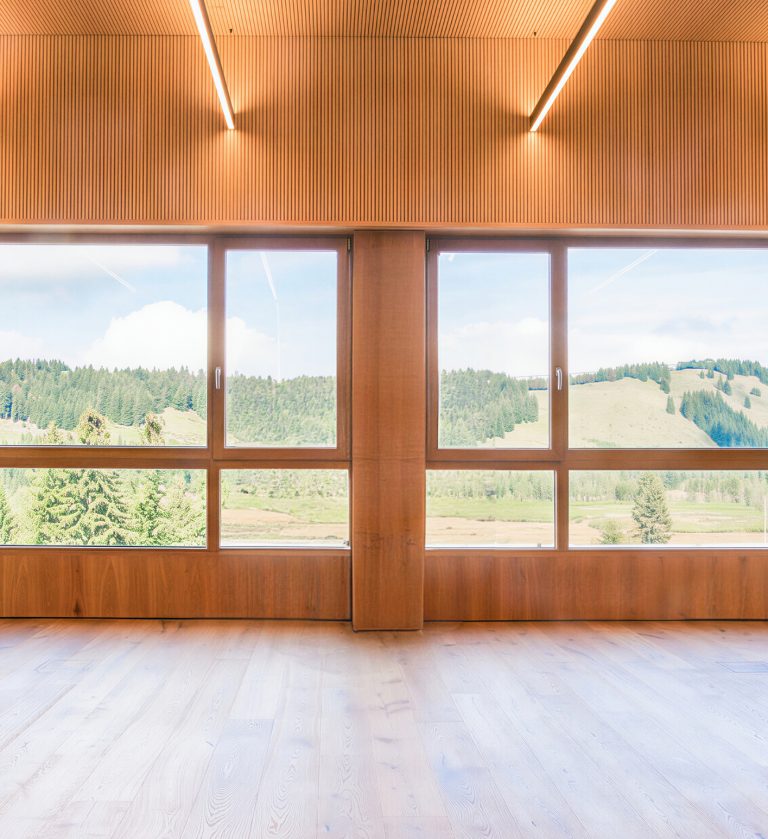 Lichtdurchfluteter Tagungsraum im Almhotel Hochhäderich mit Holzdecke und großen Panoramafenstern mit Blick über Wald und Hochmoor im Bregenzerwald