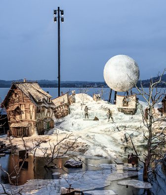 Bühnenbild der Oper Der Freischütz auf der Seebühne der Bregenzer Festspiele 2024 mit verschneitem Dorf, schiefen Fachwerkhäusern und großem Mond vor dem Bodensee