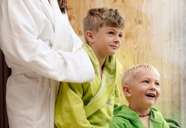 Kinderwellness im Almhotel Hochhäderich: zwei Jungen in Kinderbademänteln lachen, dahinter ist der Oberkörper der mama zu sehen.
